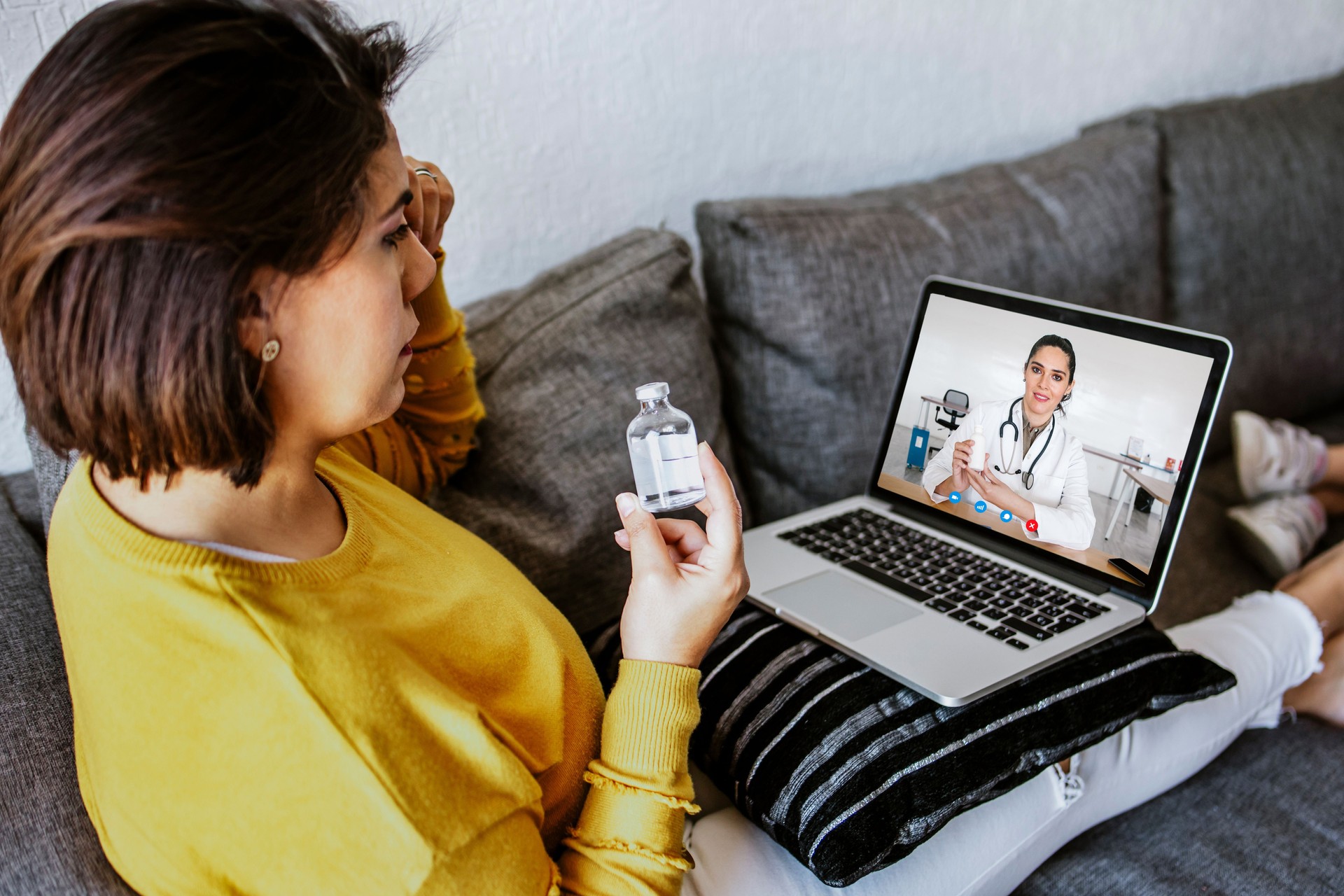 Paciente latina sentada en el sofá de casa tiene videollamada con doctora en línea en América Latina